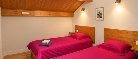 Una habitación con dos camas de madera, techo inclinado y una lámpara colgante.