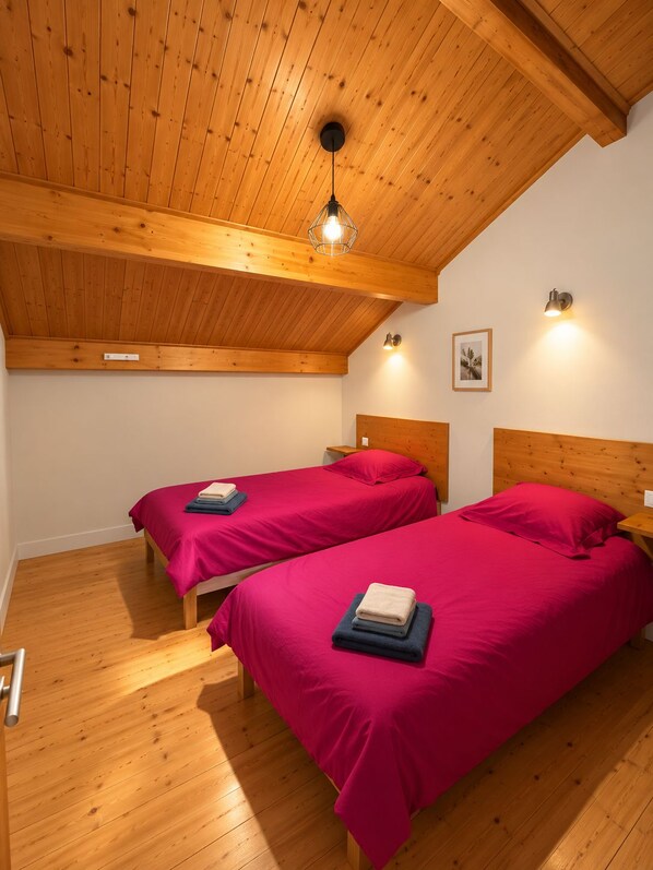 Una habitación con dos camas de madera, techo inclinado y una lámpara colgante.