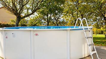 Piscina circular con escalera, rodeada de árboles y un cielo despejado.