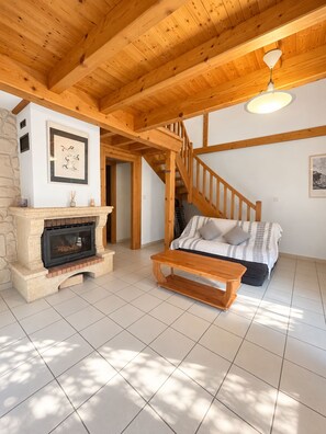 A cozy living room with a fireplace, a sofa, a wooden bench, and a staircase. - Gîte Petit Pierre Sonnay, Isère (Sonnay)