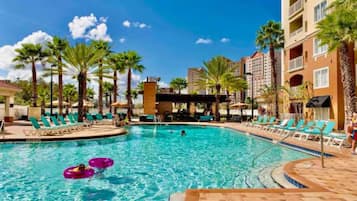 Piscina com espreguiçadeiras e palmeiras, rodeada por edifícios de hotel.