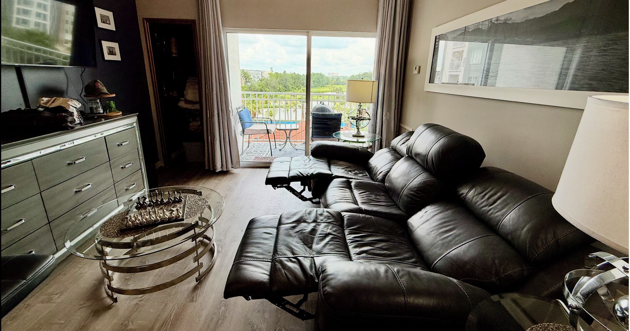 A living room with a sofa, a glass coffee table, a cabinet, and a view of the outdoors.