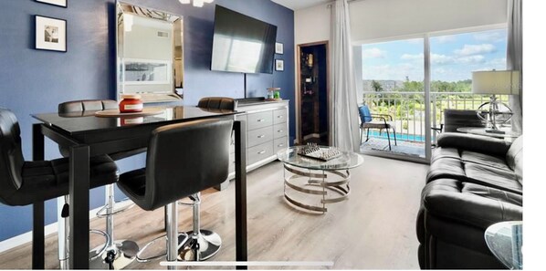 Una sala de estar moderna con comedor, un sofá, un televisor y vistas al exterior.