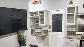 Een knus woongedeelte met een aan de muur bevestigde televisie, een klein tafeltje met een bankje, een sofa en op maat gemaakte kasten met een raam.