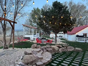 Un jardin avec une pergola en bois, des fauteuils Adirondack rouges, un chemin de pierres et un bâtiment blanc avec un toit rouge.