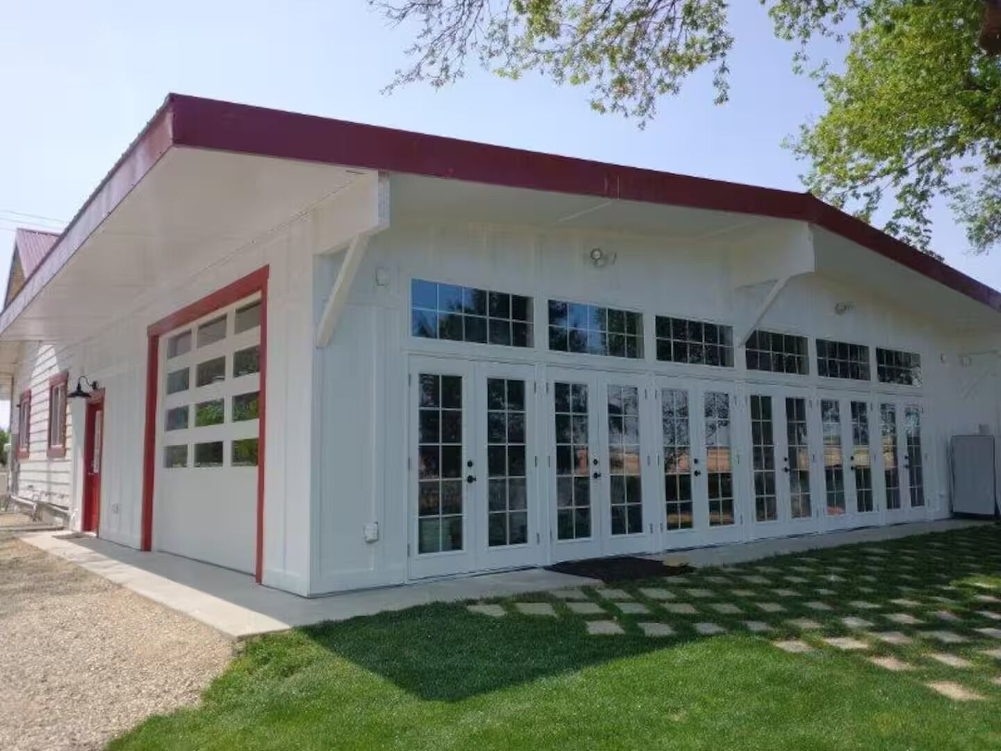 A white building with a red roof, large windows, and a garage door.