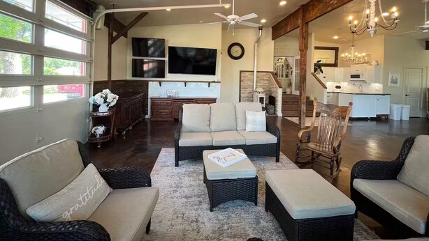 A spacious living area with a large sofa, a coffee table, and a fireplace. There is a kitchen in the background with a dining area.