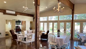 A spacious room with a polished wooden floor, a chandelier, and a dining area with white chairs and a table.