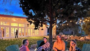 A group of people seated around a fire pit in an outdoor setting with chairs and a building in the background.