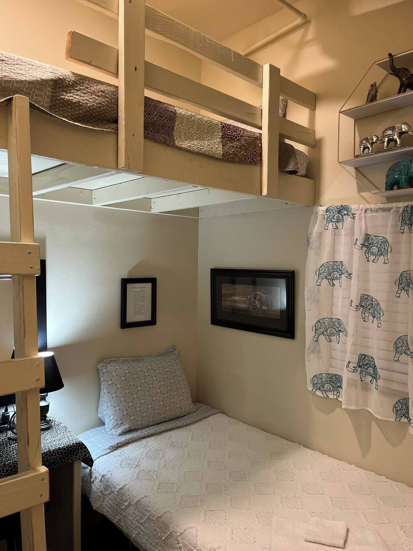 A bunk bed room with a framed picture on the wall, a patterned pillow, and a curtain with elephant designs.