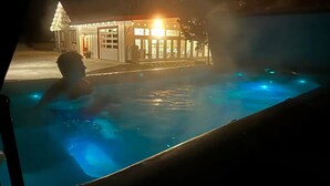 Una persona en un jacuzzi por la noche, con un edificio al fondo.