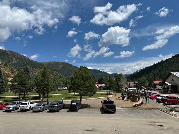 A parking lot with several cars, a playground, and buildings in the background.