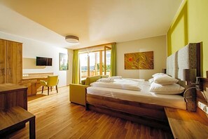 A modern hotel room with a wooden bed, a desk, a chair, and a television. - Gasthof Almblick (Strallegg)