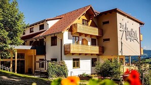 A multi-story building with a balcony, a sign reading "Hotel Alpenblick," and a view of the surrounding landscape. - Gasthof Almblick (Strallegg)