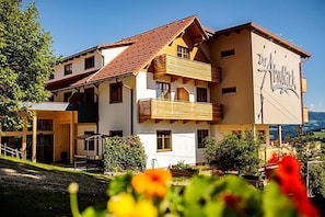 A multi-story building with a balcony, a sign reading "Hotel Alpenblick," and a view of the surrounding landscape. - Gasthof Almblick (Strallegg)