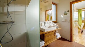 A modern bathroom with a glass shower enclosure, a large mirror, a double sink vanity, and a wooden cabinet. - Gasthof Almblick (Strallegg)