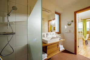 A modern bathroom with a glass shower enclosure, a large mirror, a double sink vanity, and a wooden cabinet. - Gasthof Almblick (Strallegg)