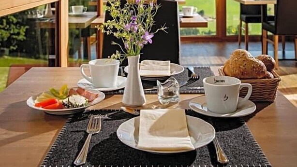 Uma mesa de jantar posta com um vaso de flores, pratos de comida e xícaras, com vista para uma paisagem deslumbrante.
