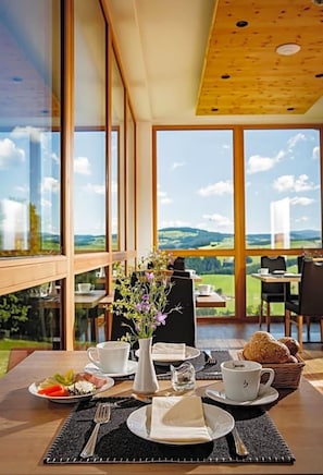 A dining table set with a vase of flowers, plates of food, and cups, overlooking a scenic landscape. - Gasthof Almblick (Strallegg)