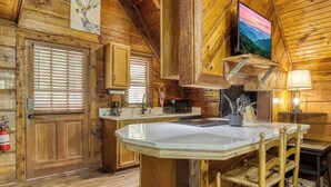 Ein rustikales Holzhaus-Interieur mit einer Küche, die eine große Kochinsel, Holzschränke, einen Kamin und einen an der Wand befestigten Fernseher zeigt.