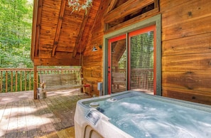 Una cabaña de madera con un jacuzzi en el porche, un banco y una puerta con marco rojo.