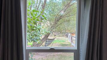 A window with curtains, a view of a tree, and a hammock.