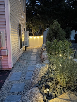 A pathway leading to a house with a covered porch area, surrounded by rocks and plants.
