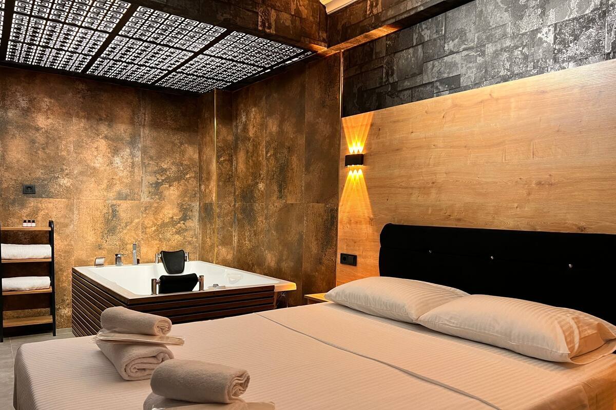 Ein modernes Hotelzimmer mit einem großen Bett, einem Holz-Kopfteil, einer integrierten Badewanne und einem außergewöhnlichen Deckengestaltung.