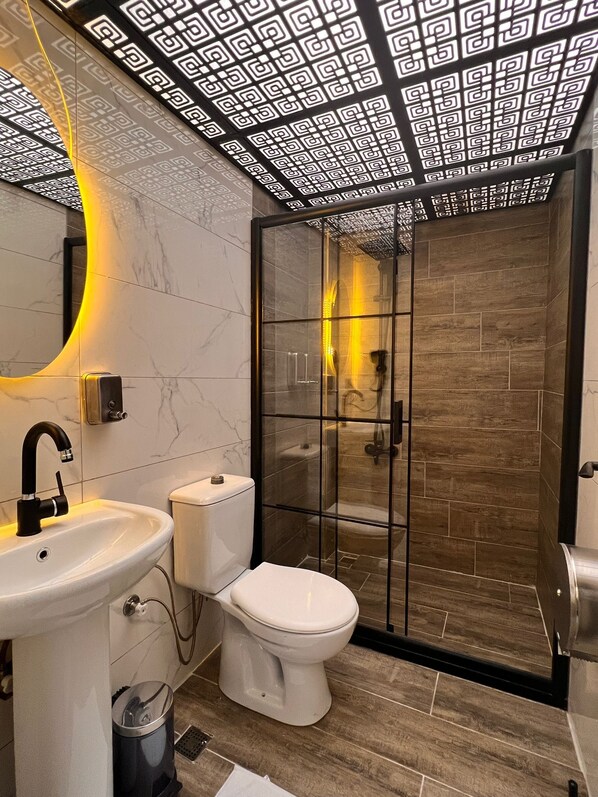 Un baño moderno con cabina de ducha de vidrio, inodoro blanco y lavamanos con encimera de mármol.