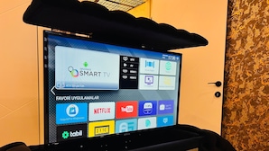 A hotel room with a TV displaying a smart TV interface, a door, and a patterned wall. - Petra Otel (Eskişehir)