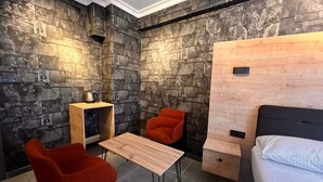 A compact room with a bed, a small table, two chairs, and a stone-textured wall. - Petra Otel (Eskişehir)