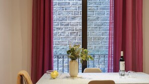 Una mesa de comedor con mantel estampado, dos sillas, un florero con planta, una botella de vino y una copa sobre la mesa.