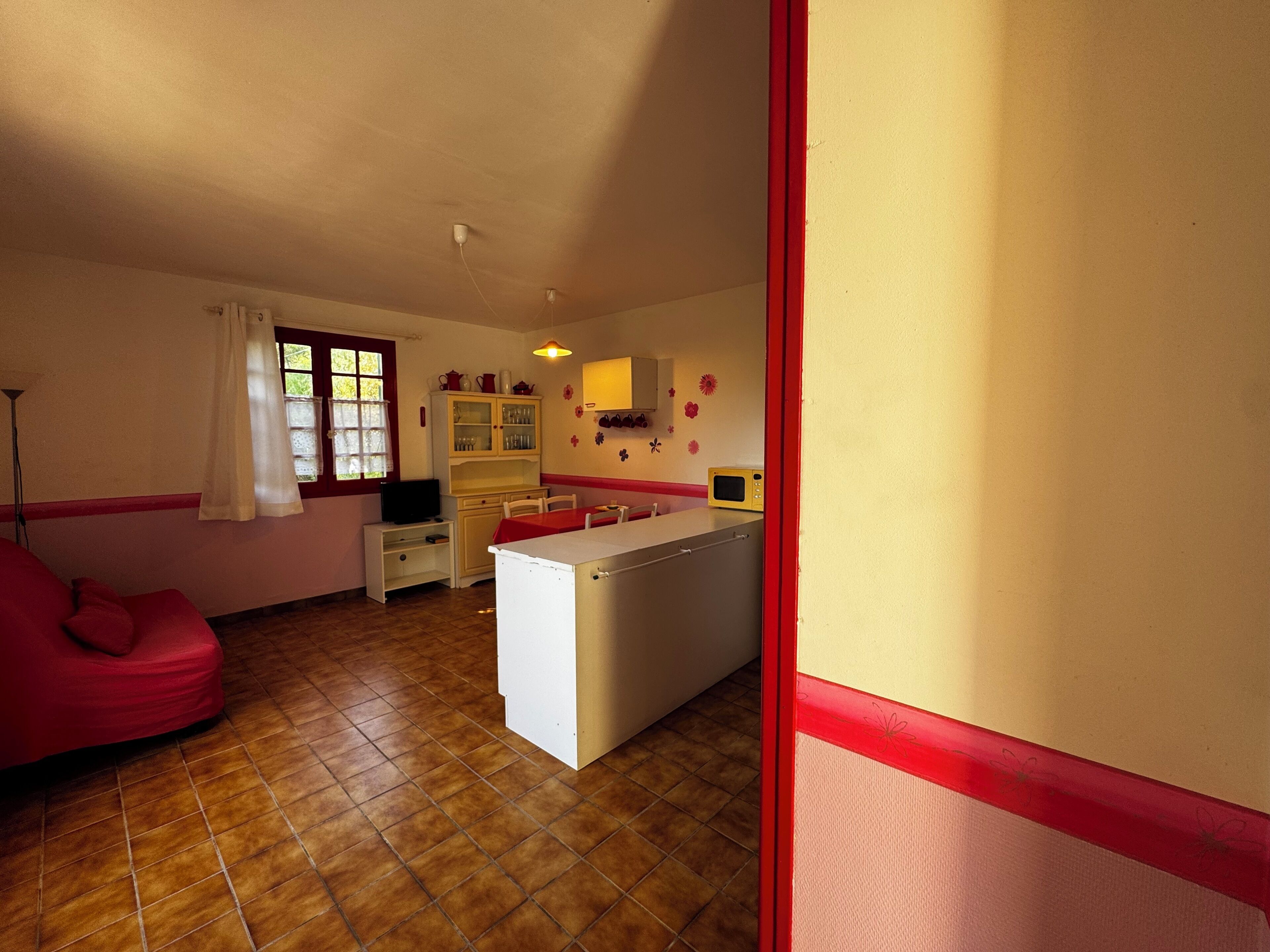 Eine kompakte Küche mit Kühlschrank, Mikrowelle und Schränken. Im Wohnbereich befindet sich ein Esstisch mit Stühlen und ein rotes Sofa.