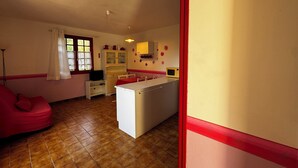 A compact kitchen with a refrigerator, microwave, and cabinets. There is a dining table with chairs and a red sofa in the living area. - House La Baixada (Oms)