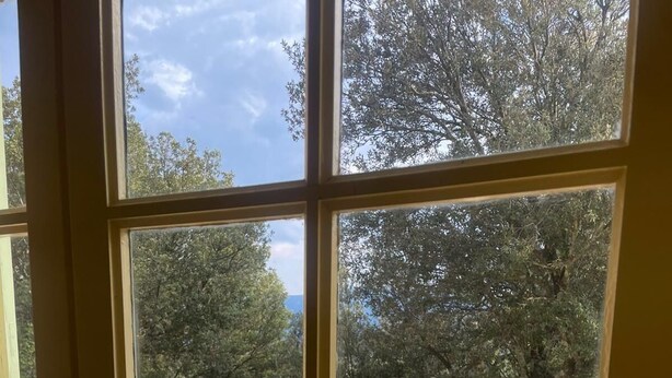 A room with a view of a balcony, a tiled floor, and a window with a view of trees and a clear sky. - House La Baixada (Oms)