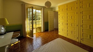 A room with a bed, a desk, a lamp, and a view of a balcony through a door. - House La Baixada (Oms)