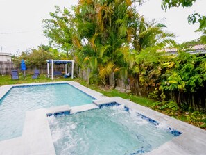 Una piscina rectangular amb un banyera d'hidromassatge al centre, envoltada de vegetació exuberant i una tanca de fusta.
