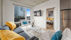 A modern living room with a gray sofa, a white coffee table, and a view of a cityscape through large windows. - ENVITAE Hotel | 2 Bedroom Luxury Apartments (Chicago)