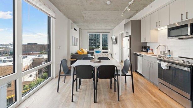A modern kitchen with a dining area, large windows, and a city view. - ENVITAE Hotel | 2 Bedroom Luxury Apartments (Chicago)