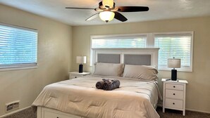 A bedroom with a bed, two bedside tables, a ceiling fan, and two windows with blinds. - SpaciousHome with King Bed, Game Room & Washer/Dryer (Hanford)