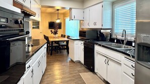A modern kitchen with white cabinets, a black countertop, and a dining area with a wooden table and chairs. - SpaciousHome with King Bed, Game Room & Washer/Dryer (Hanford)