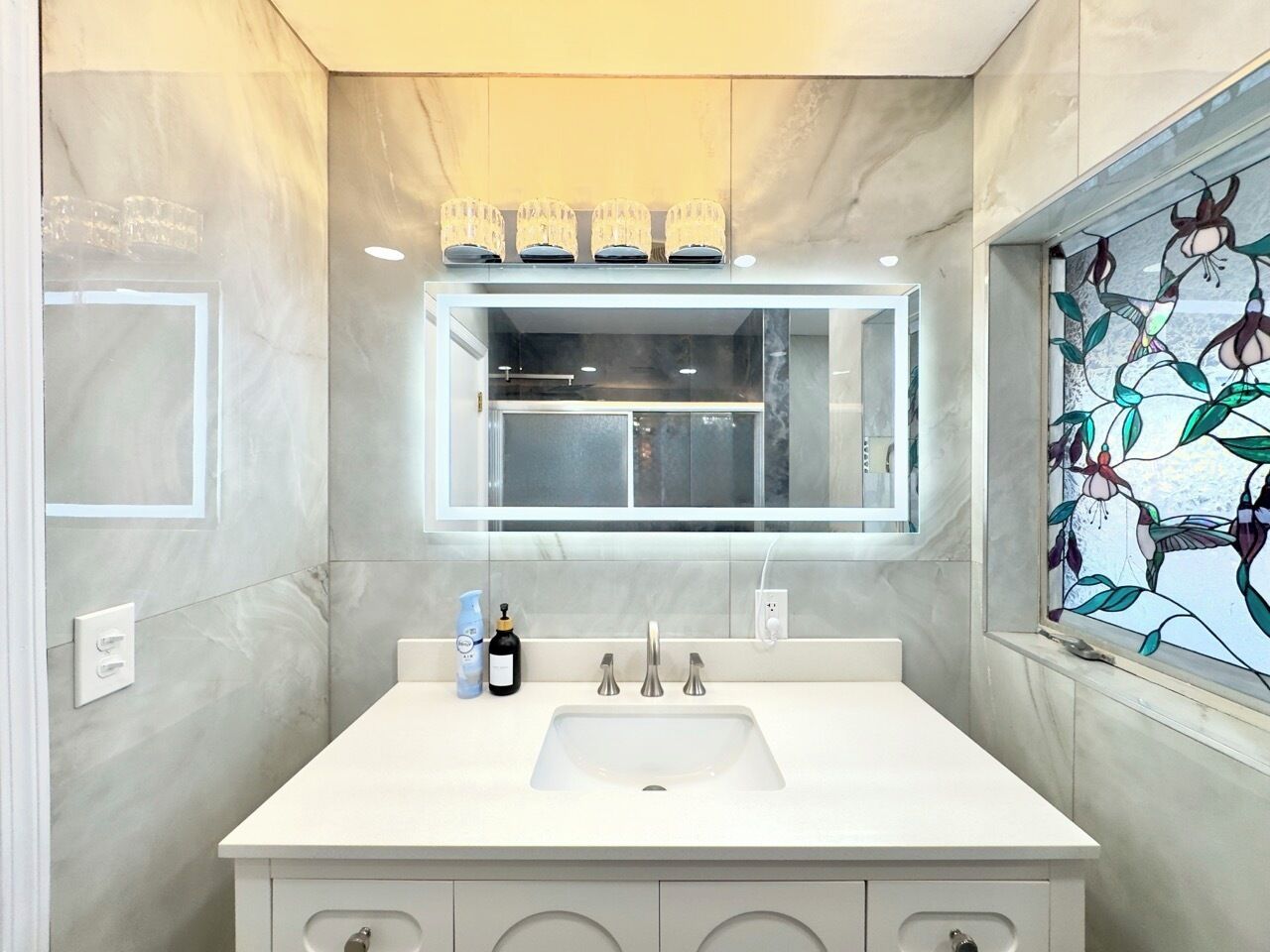 A modern bathroom with a large mirror, white sink, and marble walls.