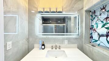 A modern bathroom with a large mirror, white sink, and marble walls.