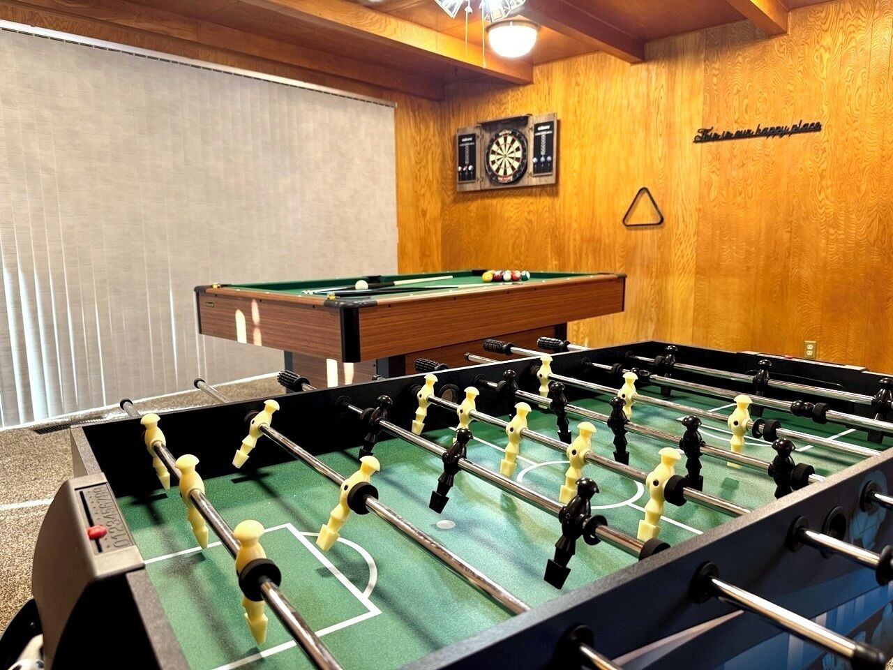 A foosball table in a room with wooden walls and a dartboard.