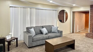 A living room with a grey sofa, a wooden coffee table, and a small side table. There is a white radiator and a circular mirror on the wall. - SpaciousHome with King Bed, Game Room & Washer/Dryer (Hanford)