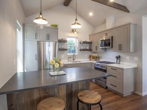 A modern kitchen with stainless steel appliances, a large island with stools, pendant lighting, and a view of the outdoors. - One bedroom one bathroom studio with full kitchen and stunning patio. (Ashland)