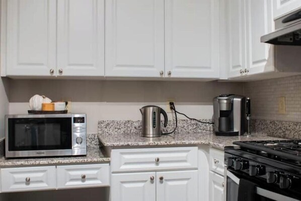 A kitchen with white cabinets, a microwave, a kettle, a coffee maker, and a stove.
