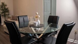 A modern living room with a glass-top dining table surrounded by black chairs, a sofa, and a potted plant. - Cozy by Airport & Downtown (Atlanta)