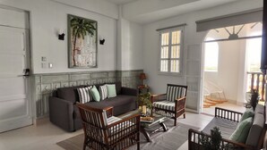 A spacious living room with a grey sofa, two striped chairs, a coffee table, and a large window with a view of the outdoors. - Apartment in the Historic Center with a great view- BARUC III (Cartagena de Indias)