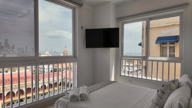 A hotel room with a bed, a TV, and large windows offering a city view. - Apartment in the Historic Center with a great view- BARUC III (Cartagena de Indias)